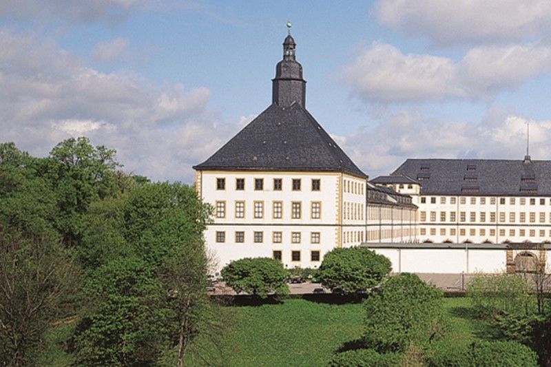 Barockschloss umgeben von grüner Landschaft und blauem Himmel