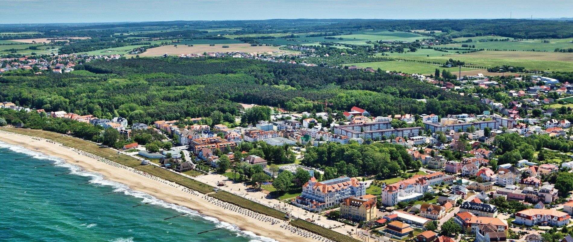 Luftaufnahme einer Küstenstadt mit Strand, Wald und umliegenden Feldern.