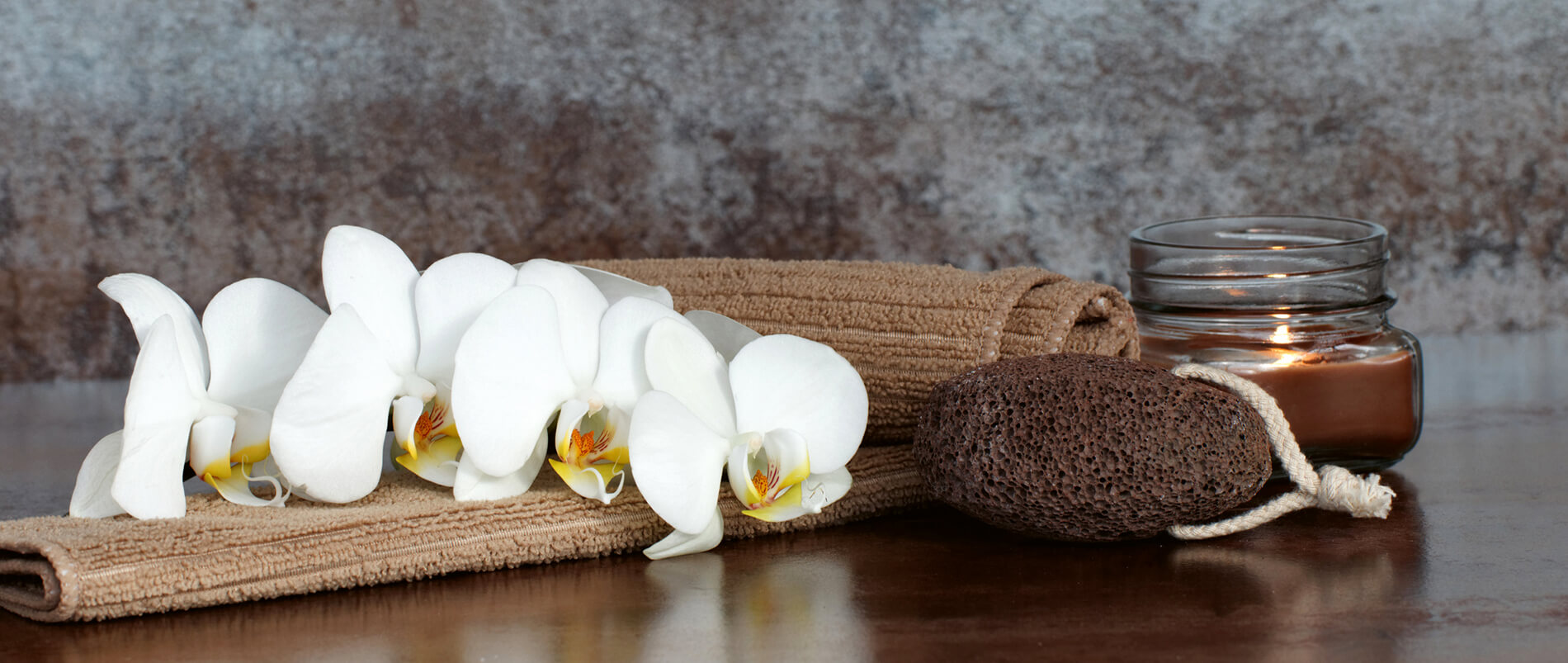 Braunes Handtuch mit weißen Orchideen, Bimsstein und brennender Kerze