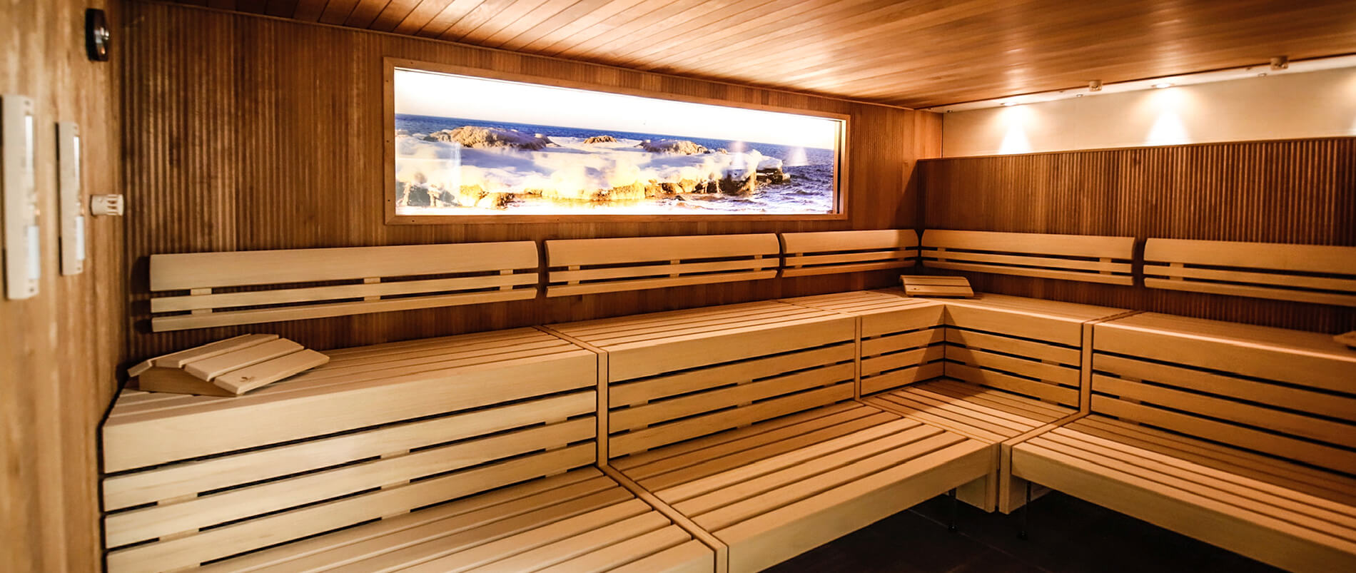 Innenraum einer modernen Sauna mit Holzbänken und einem großen Panoramafenster mit Blick auf eine felsige Küstenlandschaft.