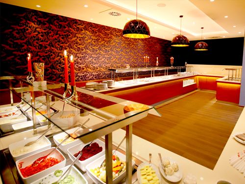 Elegantes Buffet mit leeren Servierplatten und dekorativen Elementen wie Kerzen und moderner Beleuchtung.