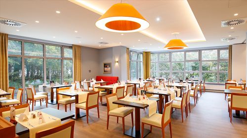 Modern eingerichtetes Restaurant mit mehreren gedeckten Tischen und großen Fenstern mit Blick ins Grüne.