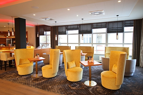 Gemütlicher Loungebereich mit gelben Sesseln und Holztischen in einem modern beleuchteten Raum.