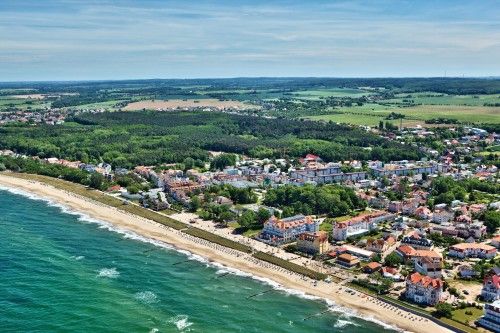 Luftaufnahme einer Küstenstadt mit Sandstrand, grünen Waldflächen und bebauten Gebieten