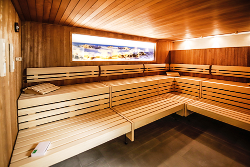 Innenansicht einer modernen Sauna mit Holzbänken und einem dekorativen Landschaftsbild an der Wand.