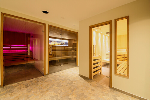 Innenansicht einer modernen Sauna mit mehreren Räumen, darunter ein Raum mit rosa Beleuchtung.
