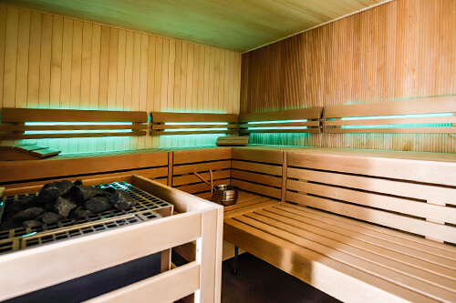 Innenansicht einer modernen Sauna mit Holzverkleidung und Sitzbänken, beleuchtet durch grünes Licht.