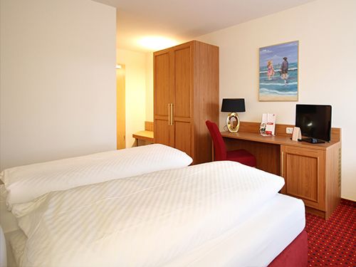 Hotelzimmer mit Doppelbett, Schreibtisch mit Lampe und Fernseher, und einem Gemälde an der Wand.