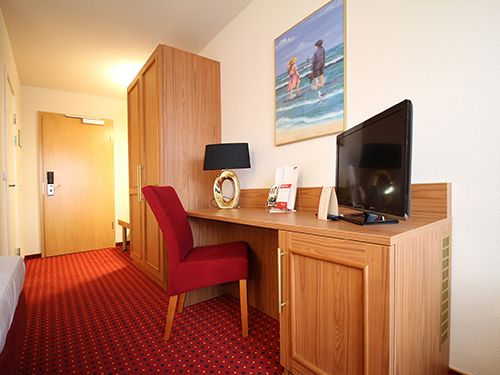 Hotelzimmer mit rotem Teppich, Holzmöbeln, Fernseher auf Schreibtisch und Wandbild.
