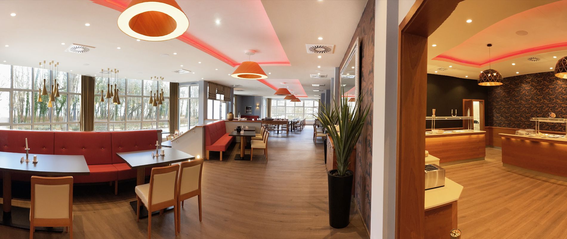 Modernes Restaurantinterieur mit roter Beleuchtung, eleganten Sitzbereichen und großen Fenstern.